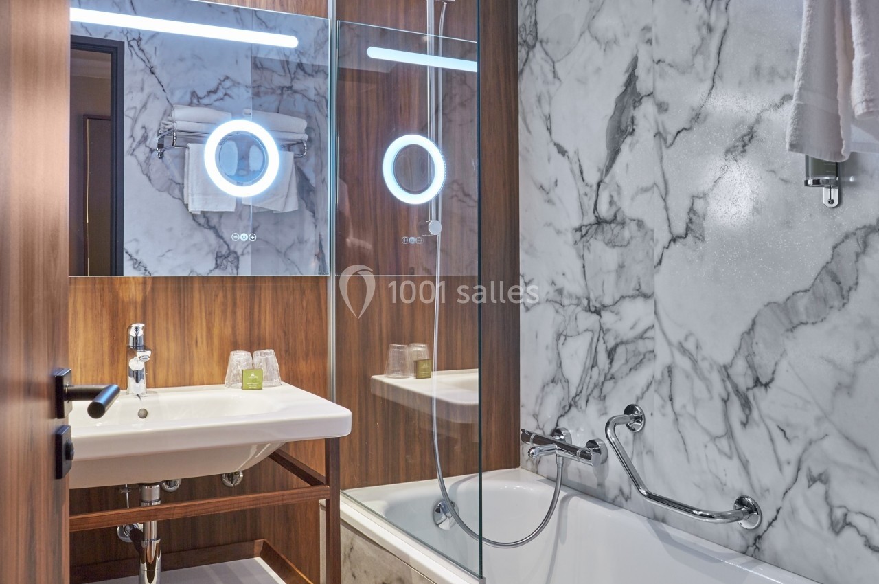 Salle de bain moderne avec lavabo, miroir éclairé, baignoire et murs en marbre.