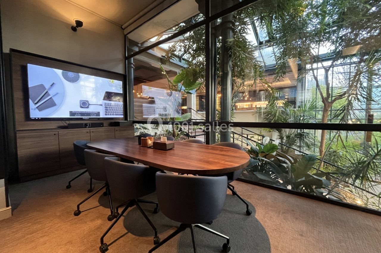 Salle de réunion moderne avec table en bois, chaises noires et grande baie vitrée donnant sur un espace végétalisé.