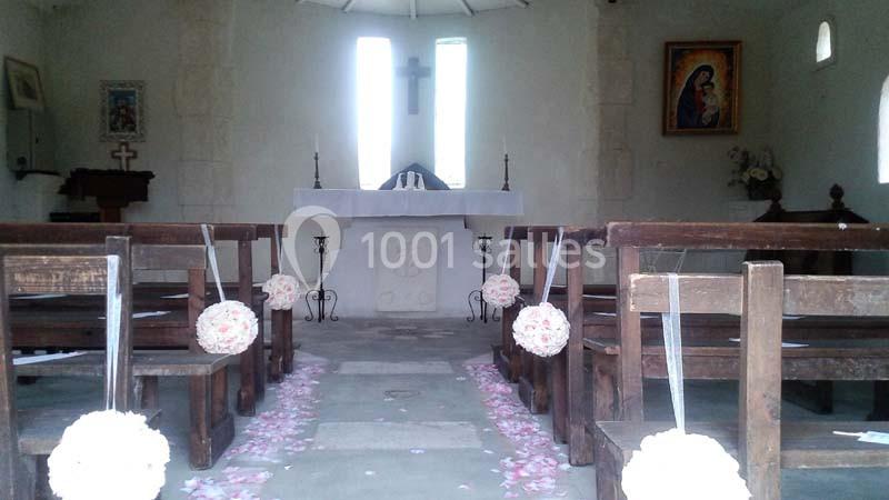 Intérieur d'une petite chapelle décorée pour un mariage, avec des bancs ornés de fleurs et un autel en arrière-plan.