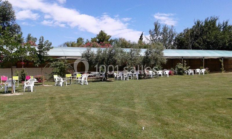 Chaises et tables disposées sur une pelouse devant une structure couverte, entourées d'arbres et de végétation.