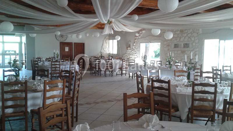 Salle de réception décorée avec des tables dressées, des chaises en bois et des drapés suspendus au plafond.
