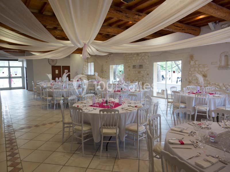 Salle de réception décorée avec des tables rondes, nappes blanches, chaises assorties et voilages suspendus au plafond.