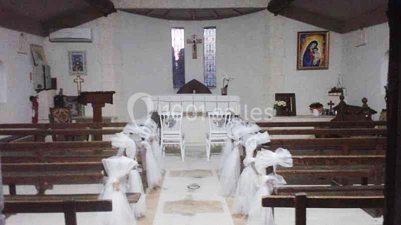Intérieur d'une petite chapelle avec des bancs décorés de nœuds blancs et un autel en arrière-plan.