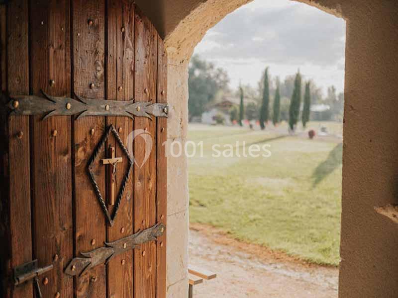 Porte en bois ouverte donnant sur un jardin ensoleillé avec pelouse, arbres et allée en arrière-plan.
