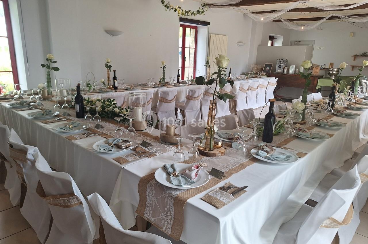Salle décorée pour un mariage avec des tables dressées, nappes blanches, chemins de table beige et éléments floraux.