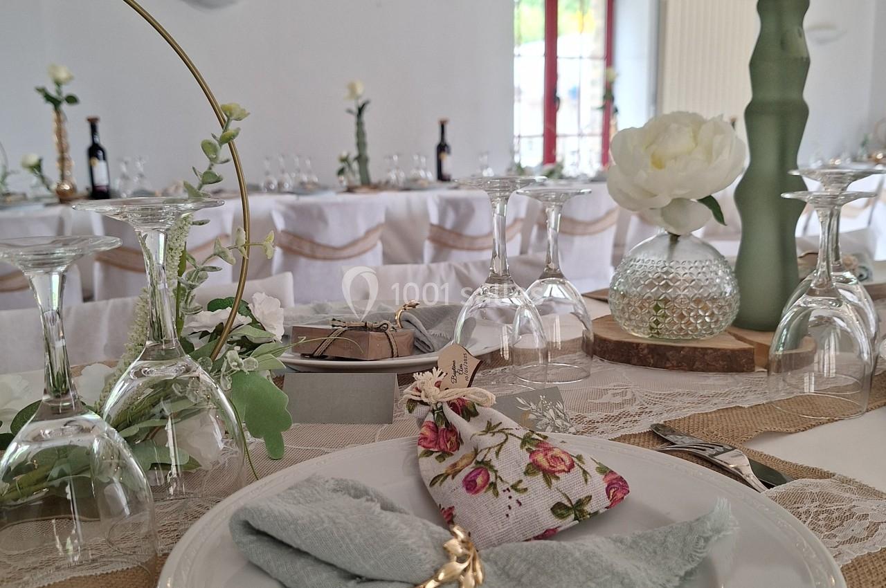 Table décorée pour un mariage avec assiette, serviette pliée, rond de serviette doré et détails floraux élégants.