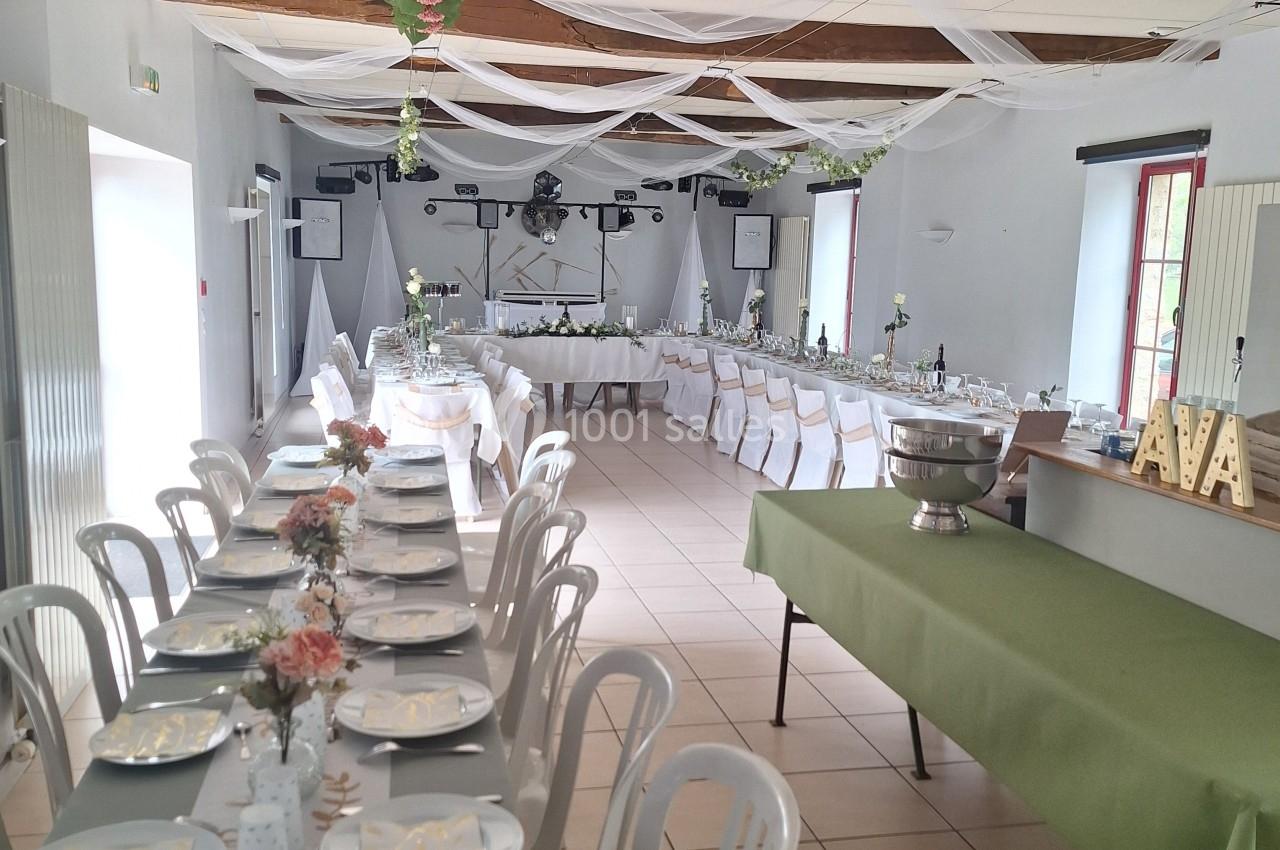 Salle décorée pour un événement avec tables dressées, nappes vertes, chaises blanches et guirlandes suspendues.