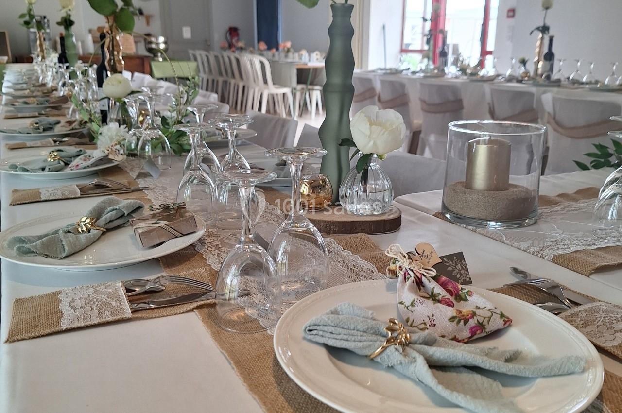 Table décorée pour un événement, avec nappes en toile de jute et dentelle, vaisselle élégante et fleurs blanches.
