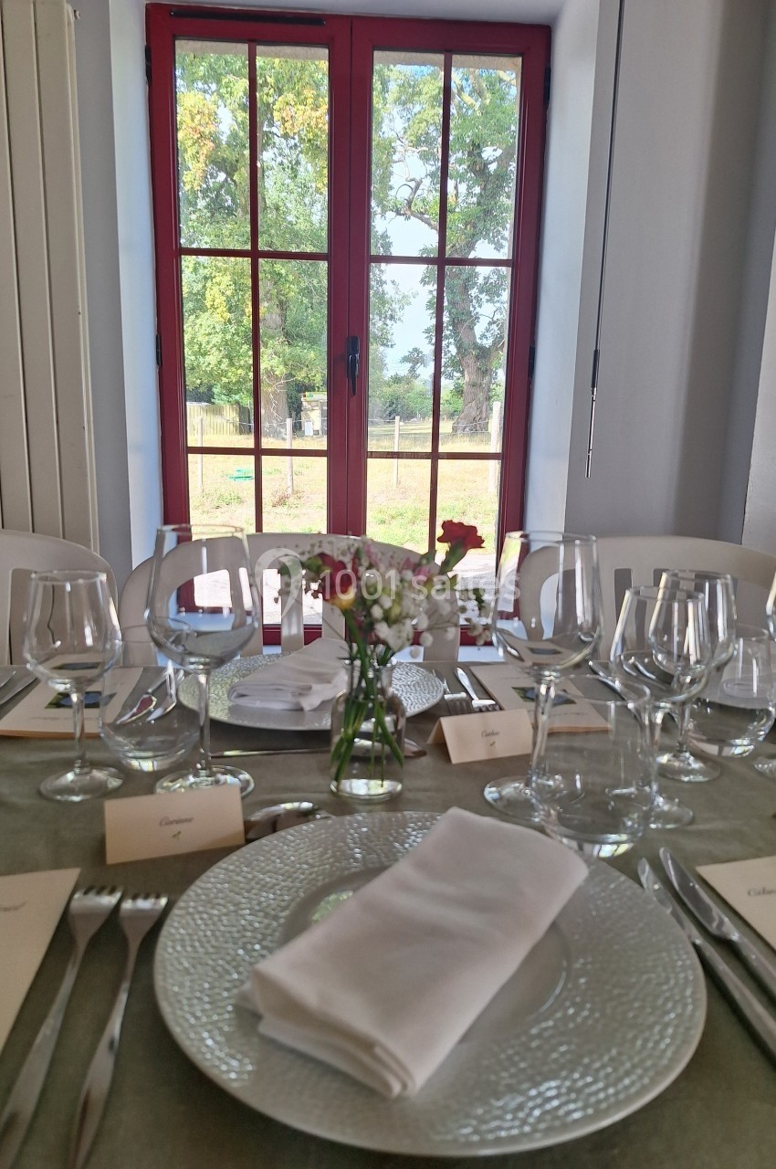 Table dressée avec vaisselle élégante, serviettes blanches, fleurs au centre, devant une fenêtre donnant sur un jardin.