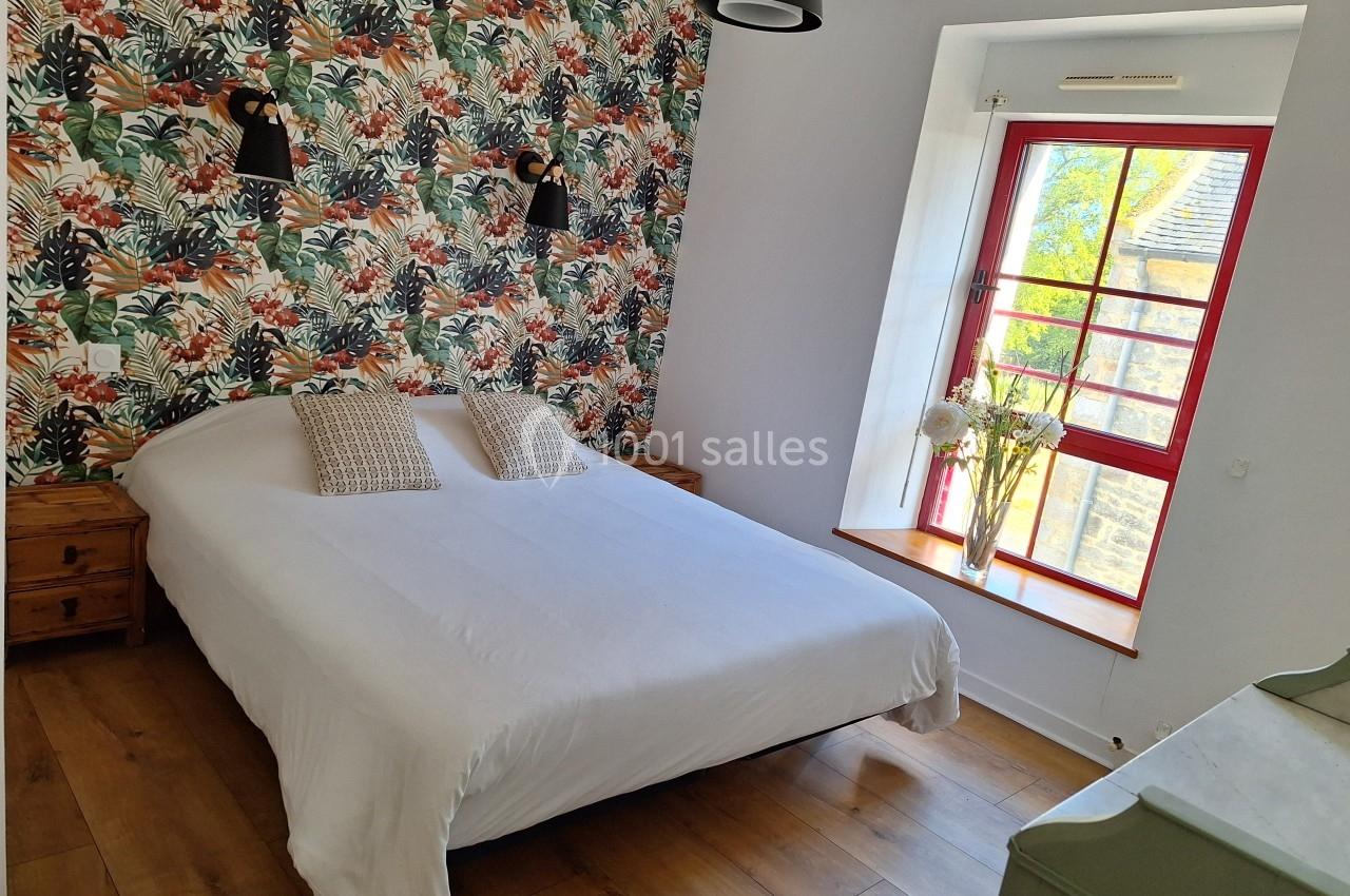 Chambre lumineuse avec lit double, mur à motifs tropicaux, parquet en bois et fenêtre donnant sur l'extérieur.