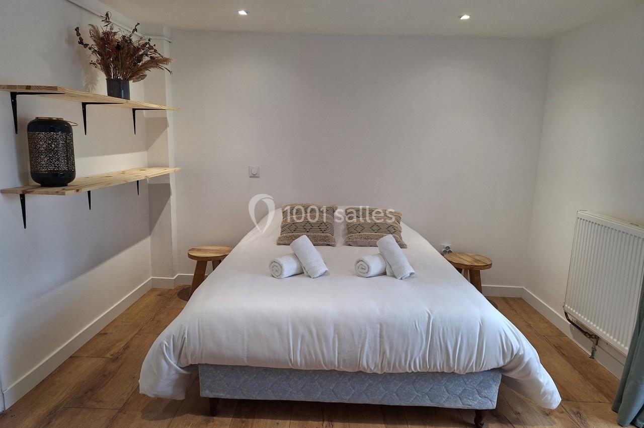 Chambre lumineuse avec un lit double, draps blancs, coussins décoratifs, étagères en bois et sol en parquet.