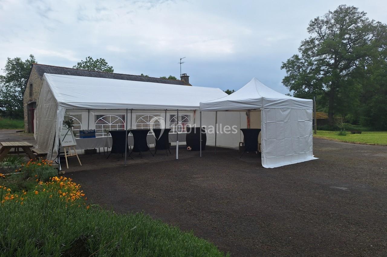 Deux tentes blanches installées en extérieur sur une surface asphaltée, entourées de verdure et de fleurs.