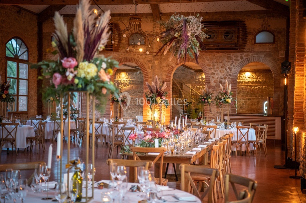 Salle de réception décorée avec des tables dressées, des bouquets floraux et des suspensions végétales.