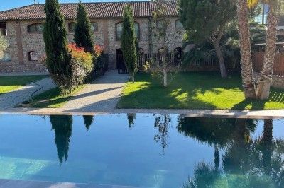 Chaises longues alignées devant un mur en pierre, entourées de grands arbres sous un ciel bleu clair.