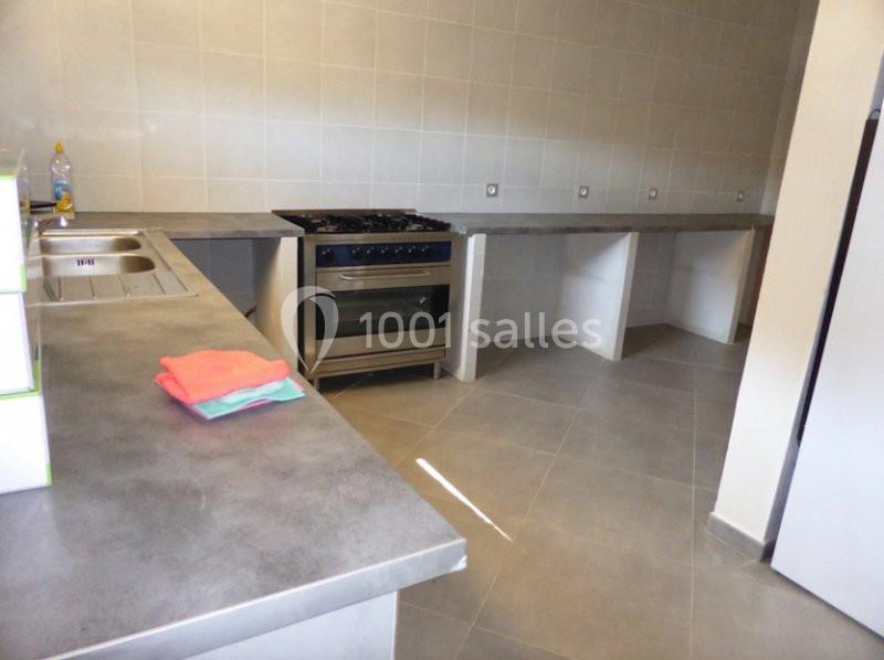 Cuisine avec plan de travail en béton, évier double, cuisinière à gaz et carrelage mural et au sol.