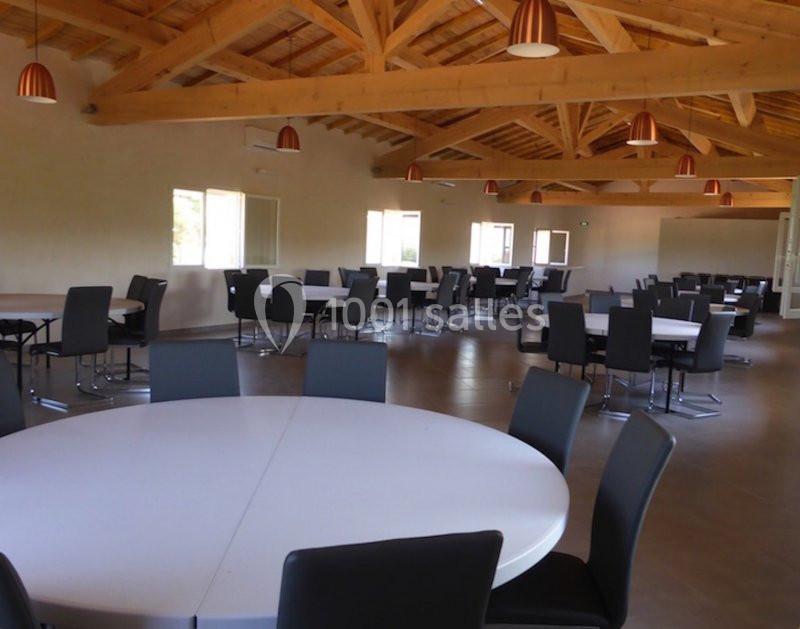 Salle spacieuse avec des tables rondes blanches et des chaises noires, éclairée par des suspensions et la lumière naturelle.