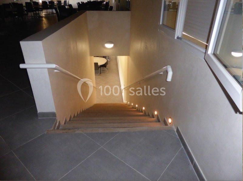 Escalier intérieur en bois avec rampes blanches, éclairé par des spots muraux et une lampe au plafond.