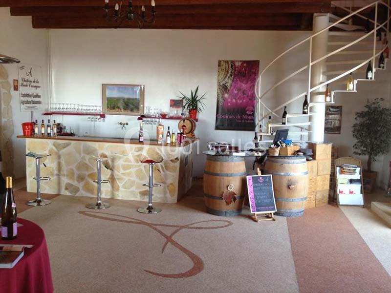 Intérieur d'une cave à vin avec un comptoir en pierre, des tabourets, des tonneaux et un escalier en colimaçon.