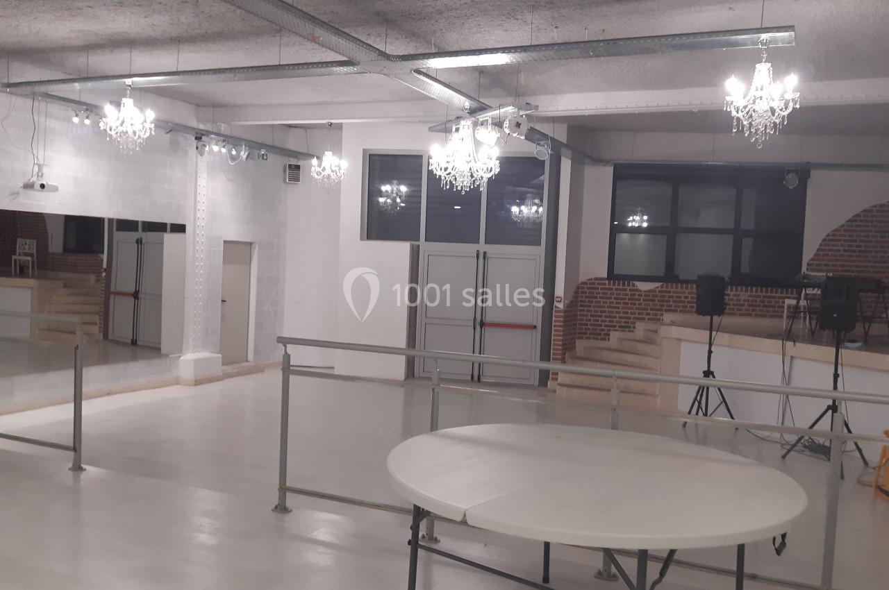 Salle lumineuse avec sol clair, miroirs muraux, murs en briques et lustres suspendus, équipée de rampes d'accès.