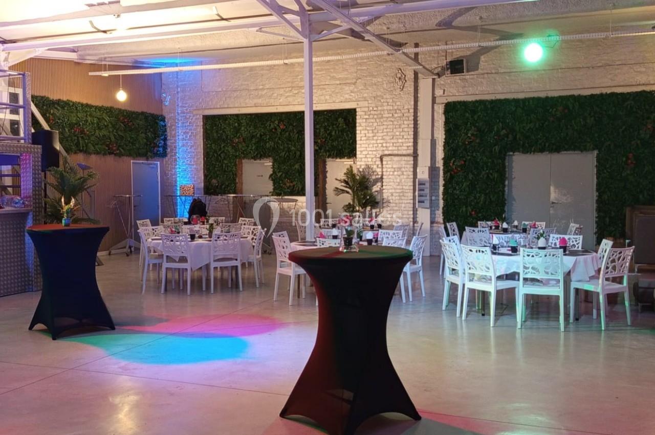 Salle de réception moderne avec tables dressées, murs végétalisés et éclairages colorés.