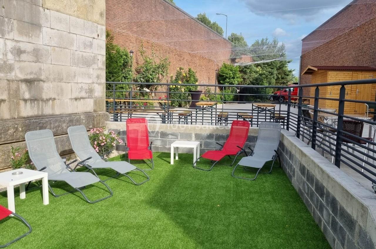 Chaises longues rouges et grises disposées sur une terrasse en gazon synthétique, entourée de murs et de balustrades.