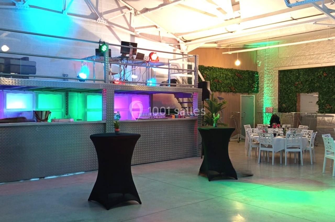 Salle moderne avec mezzanine, éclairages colorés, tables dressées et plantes décoratives.