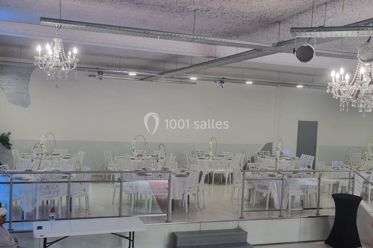Salle de réception avec tables dressées, chaises blanches et lustres suspendus dans un décor moderne et épuré.