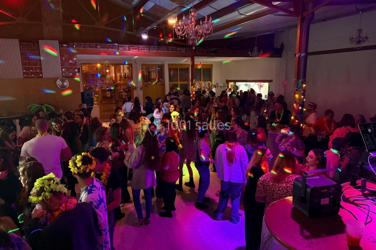 Salle festive remplie de personnes dansant sous des lumières colorées, avec une ambiance conviviale et animée.