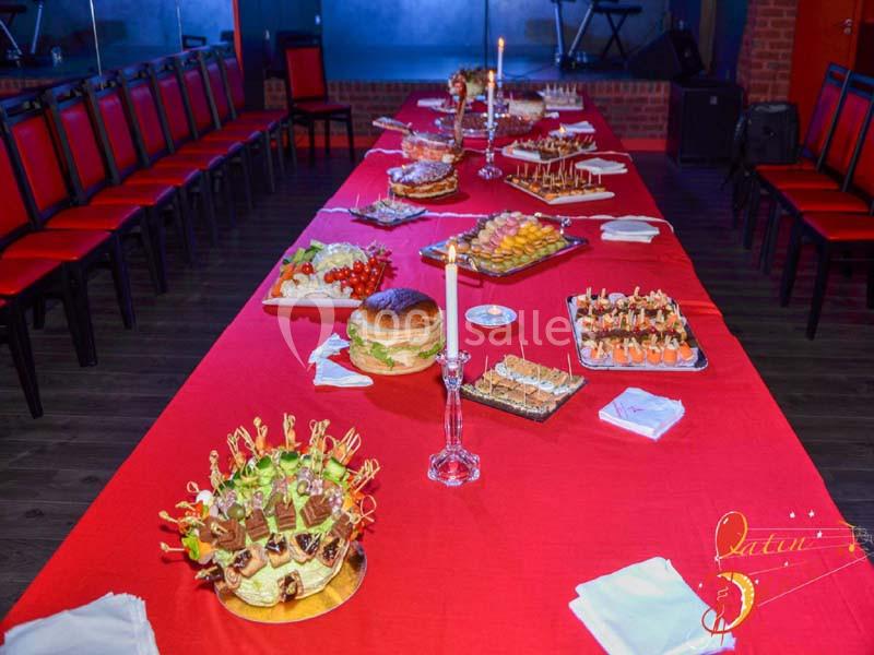 Buffet varié disposé sur une longue table rouge, avec des chandeliers et des chaises alignées autour.