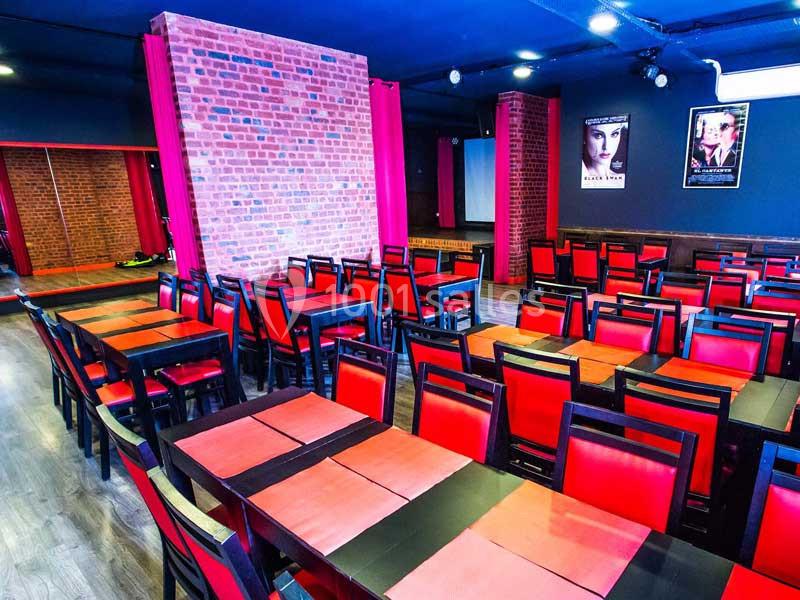 Salle avec des tables et chaises rouges alignées, murs en briques rouges et affiches de cinéma accrochées.