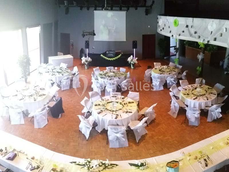 Salle de réception décorée avec des tables rondes nappées de blanc, chaises ornées de nœuds et décorations florales.