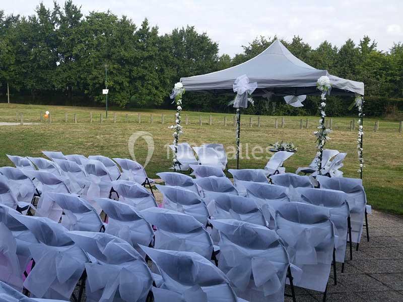 Chaises blanches décorées et disposées en rangées devant une arche de mariage ornée de fleurs, en extérieur.