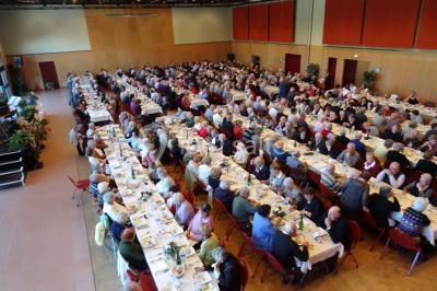 Salle de réception animée avec de nombreuses personnes debout, éclairage chaleureux et décorations suspendues.