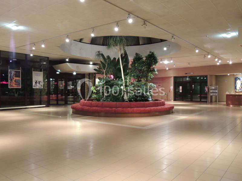 Hall spacieux avec un sol en carrelage clair, un grand îlot végétalisé central et des éclairages suspendus.