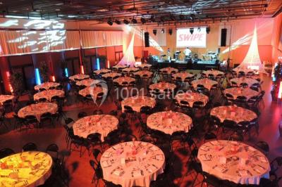 Salle de réception animée avec de nombreuses personnes debout, éclairage chaleureux et décorations suspendues.