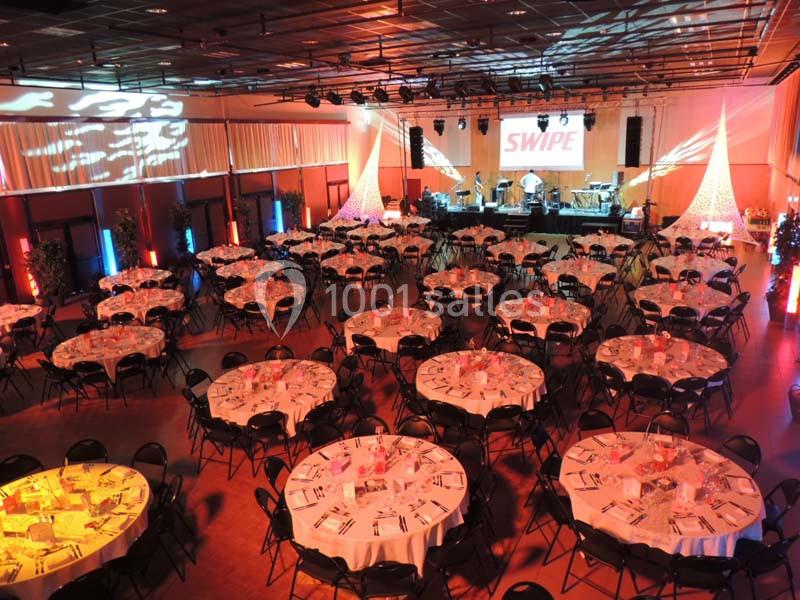 Salle de réception décorée avec des tables rondes dressées, éclairages colorés et une scène en fond avec écran.