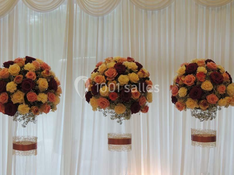 Trois arrangements floraux ronds composés de roses colorées, suspendus devant un rideau blanc plissé.