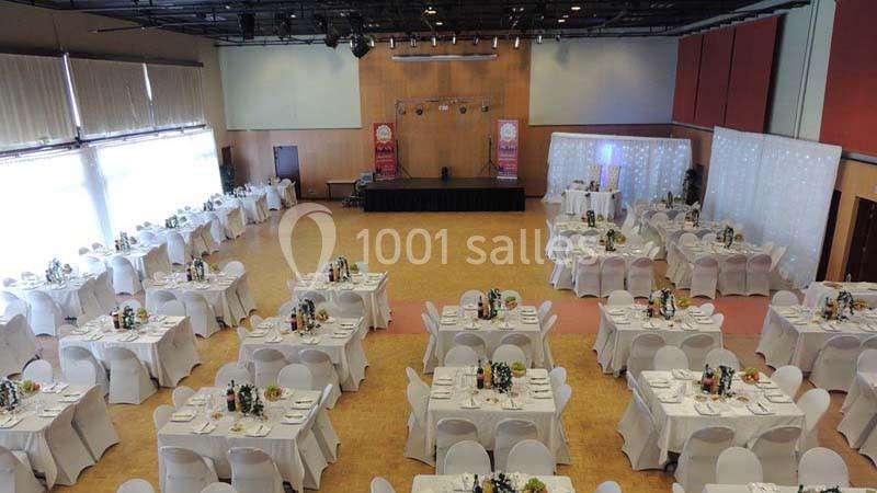 Salle de réception aménagée avec des tables rondes dressées, nappes blanches et décorations florales.