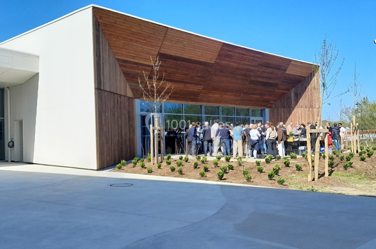Groupe de personnes rassemblées devant un bâtiment moderne avec façade en bois et grandes baies vitrées.