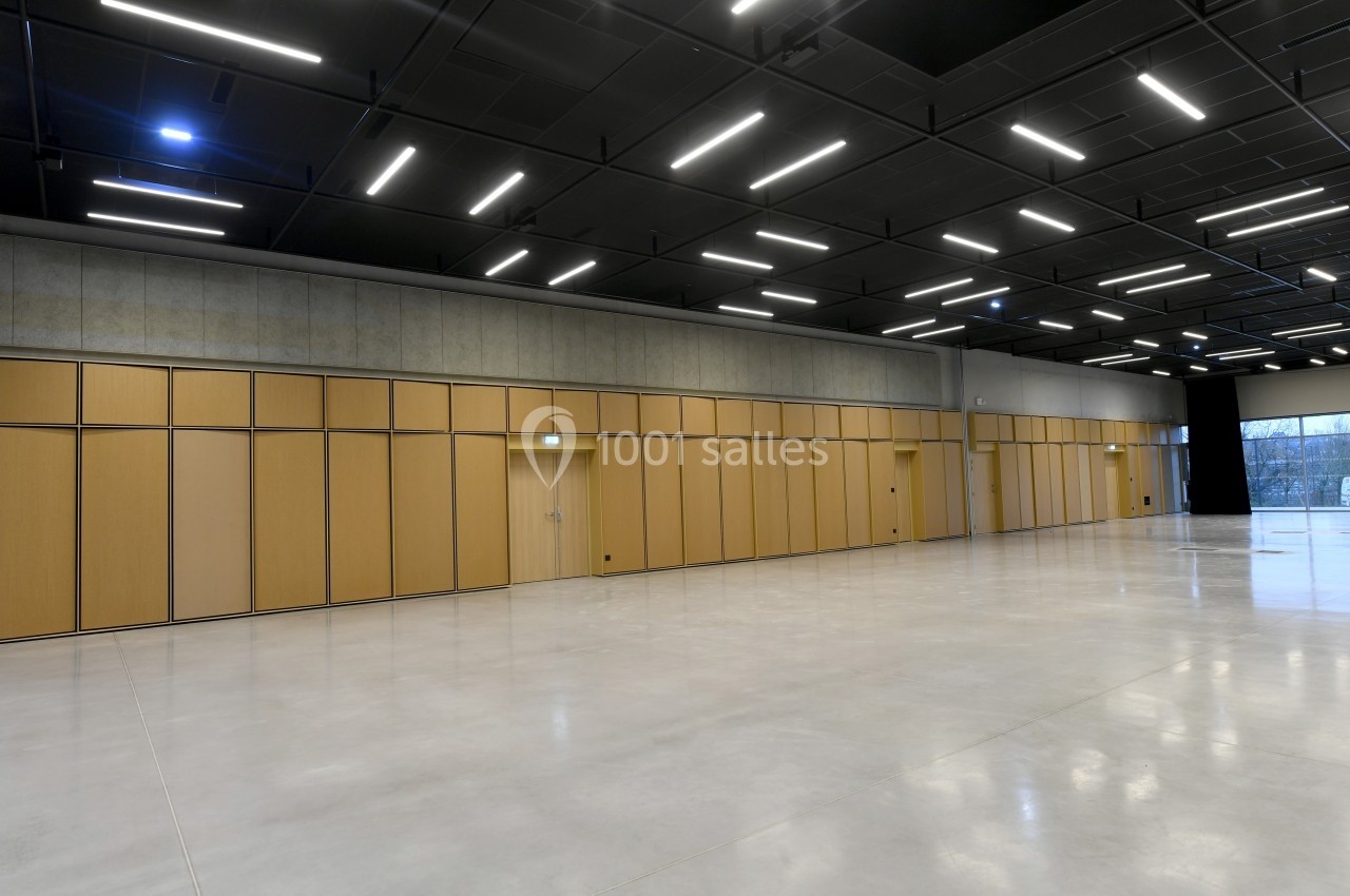 Salle vide avec sol en béton poli, murs en panneaux de bois clair et plafond noir avec éclairage LED rectangulaire.