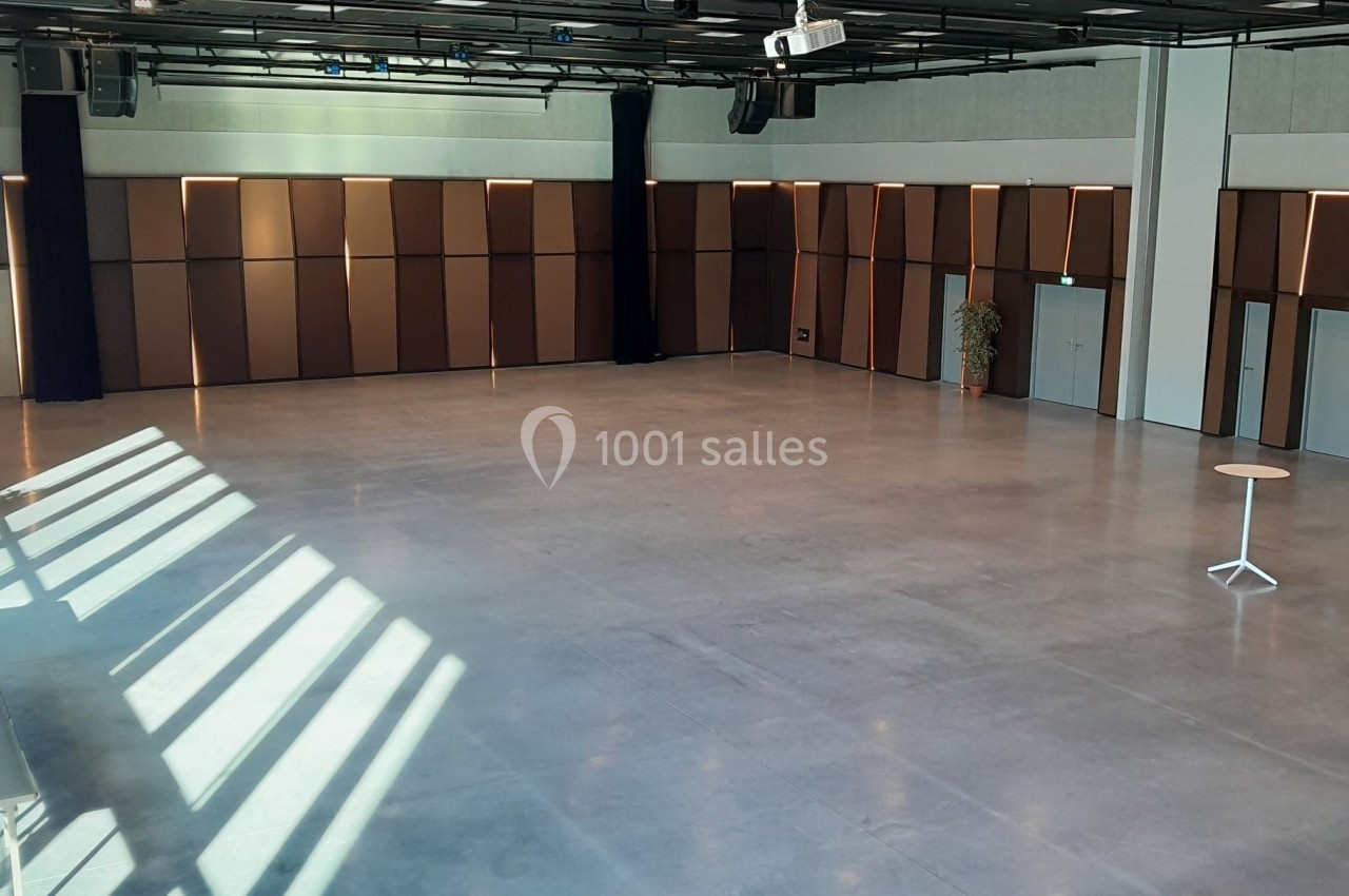 Salle vide avec sol en béton, murs en panneaux bruns, éclairage naturel et quelques plantes en pot.