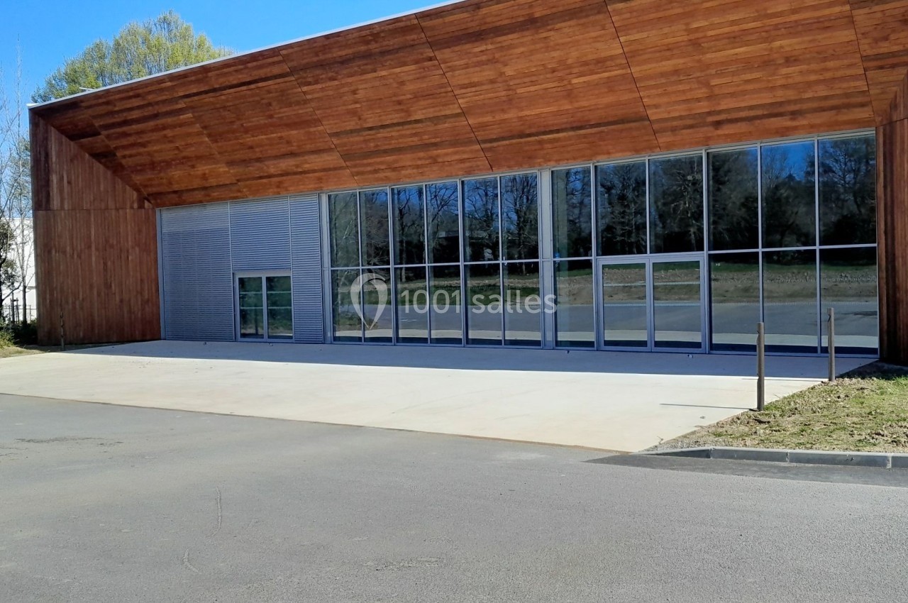Façade d’un bâtiment moderne avec revêtement en bois, grandes baies vitrées et espace extérieur dégagé.