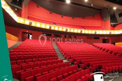 Salle de réception avec tables rondes dressées, éclairage coloré et scène équipée pour un événement.