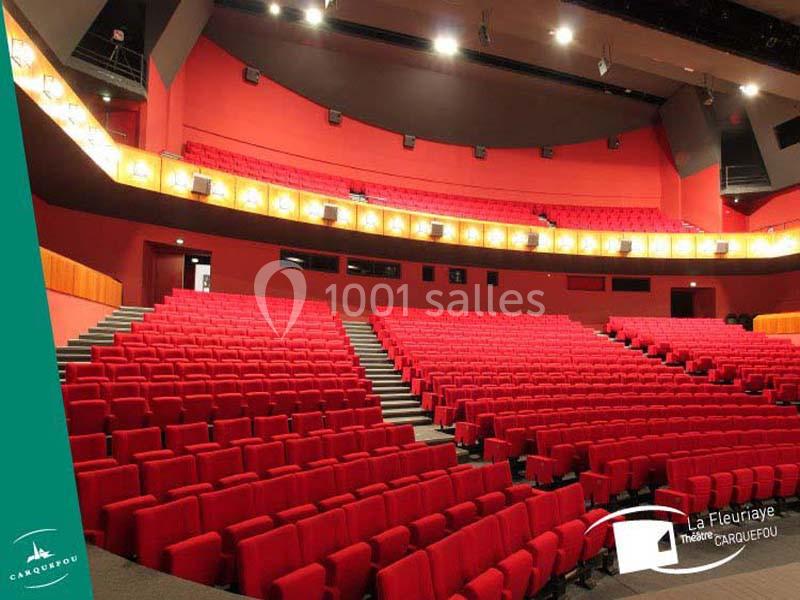 Salle de théâtre moderne avec rangées de sièges rouges vides et éclairage chaleureux.