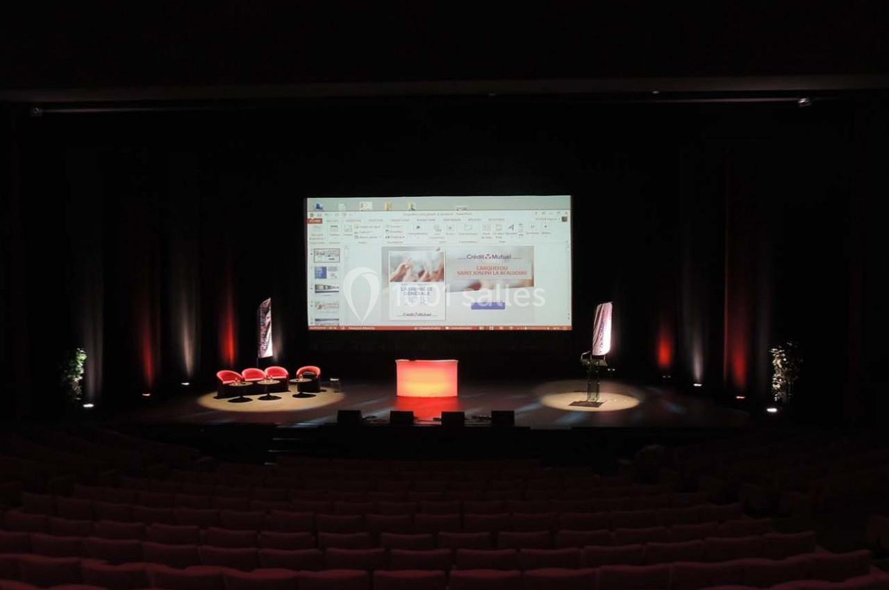 Salle de conférence sombre avec un écran de présentation allumé, un pupitre éclairé et des sièges vides.