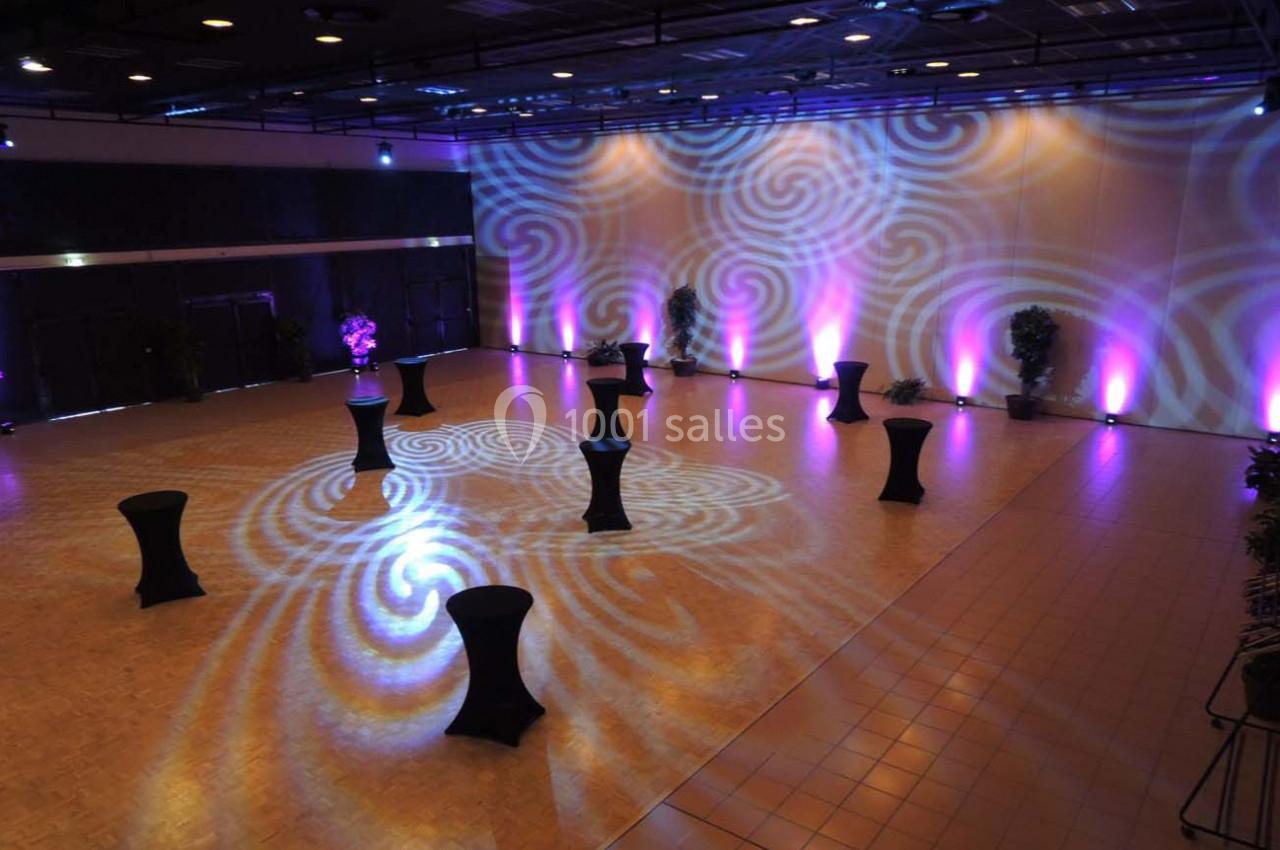 Salle de réception avec éclairage coloré, tables hautes noires et motifs lumineux projetés au sol.