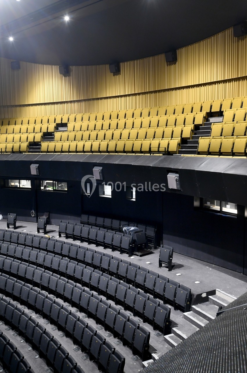 Salle de spectacle vide avec sièges noirs et jaunes, scène non visible, éclairage intérieur discret.