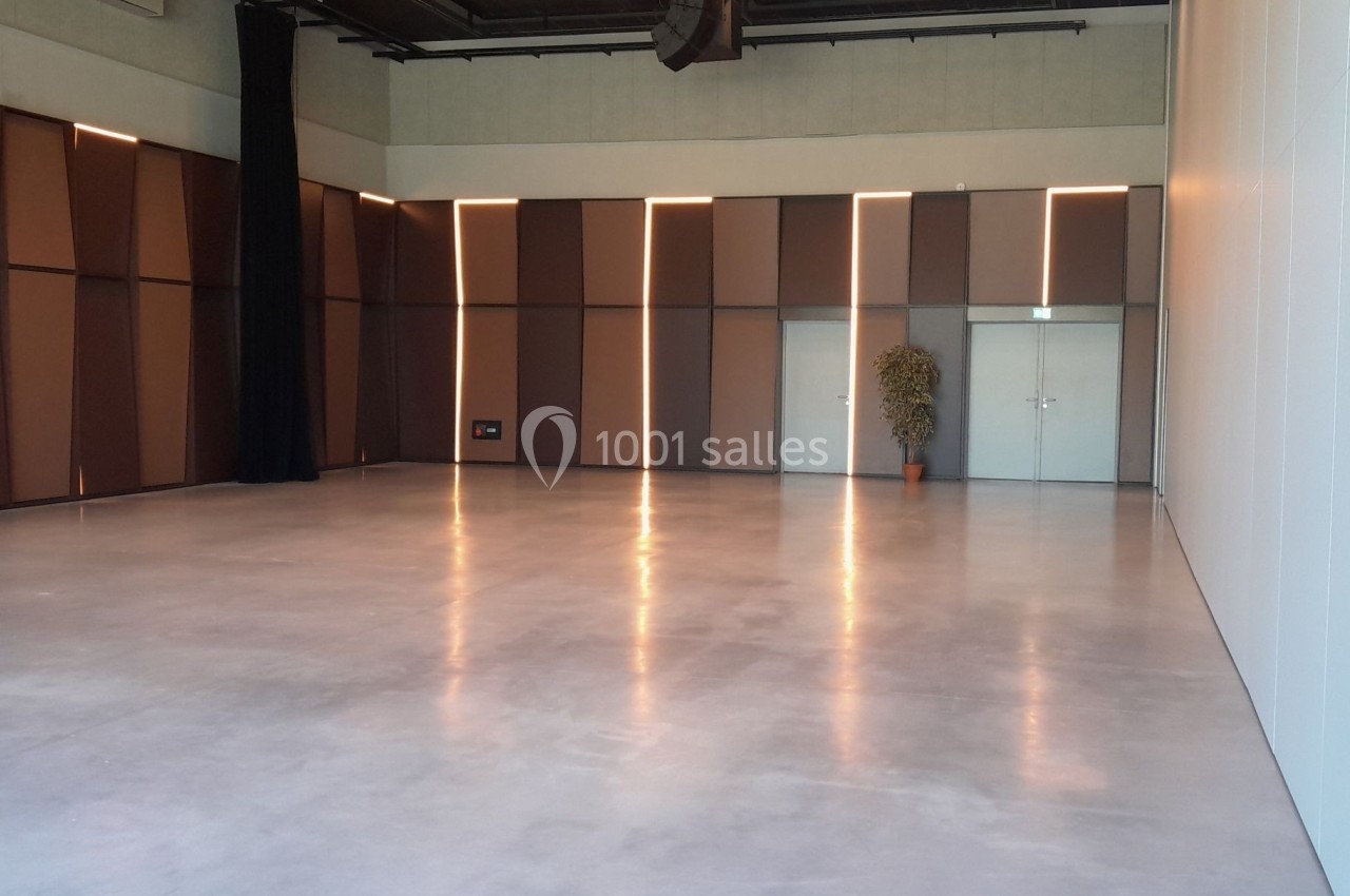 Salle vide avec sol en béton poli, murs bruns et blancs, éclairage doux et une plante près des portes blanches.