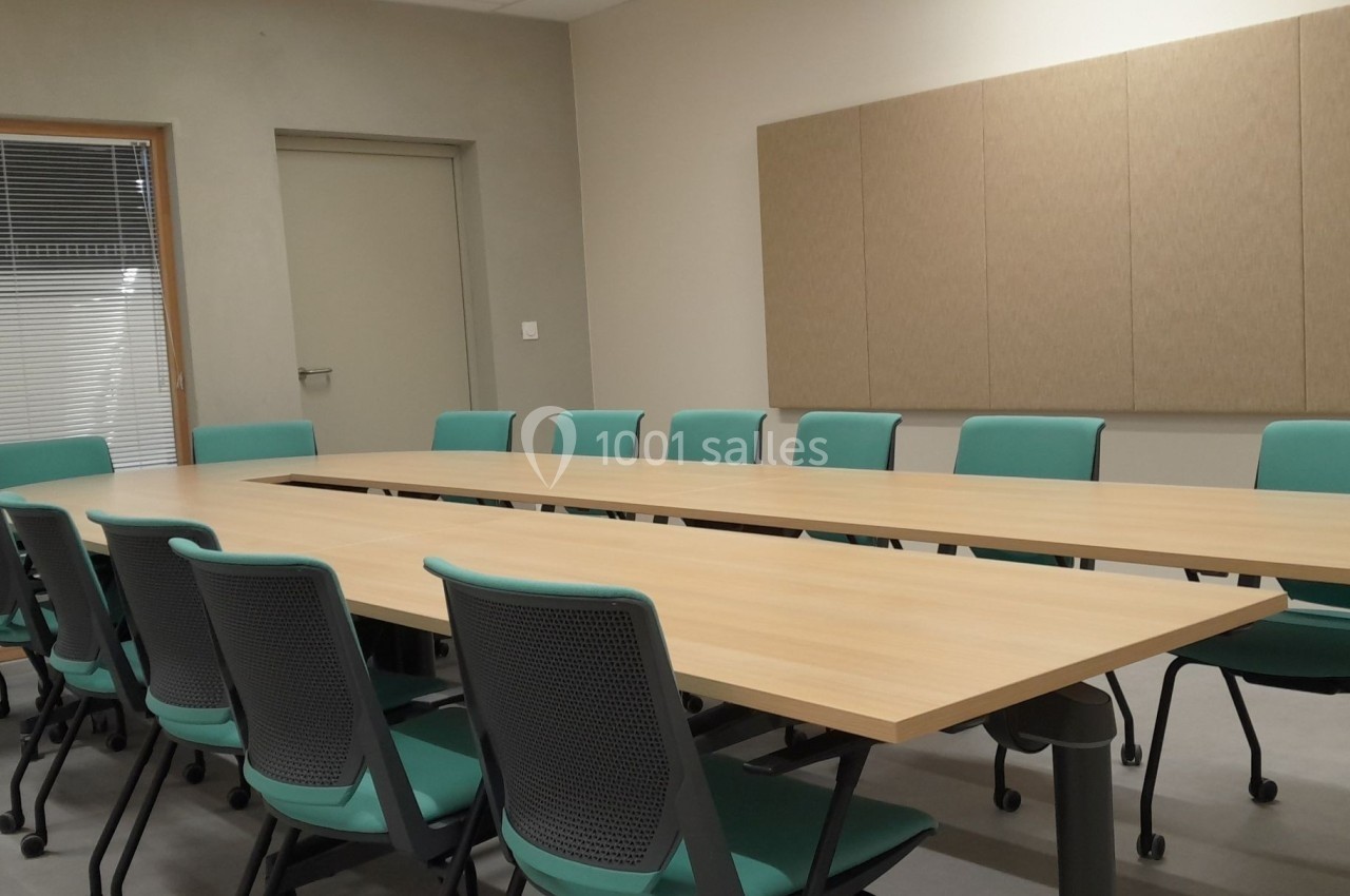 Salle de réunion avec une grande table en bois entourée de chaises vertes et un mur équipé de panneaux acoustiques.