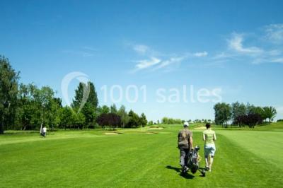 Paysage de terrain de golf avec pelouses verdoyantes, drapeau sur le green et maisons en arrière-plan.
